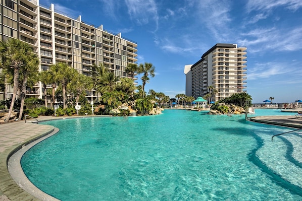 A large outdoor swimming pool surrounded by palm trees and hotel buildings.