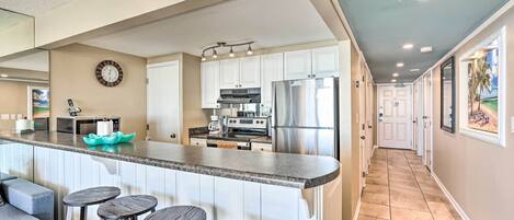 A modern kitchen with white cabinets, stainless steel appliances, and a bar area with stools.