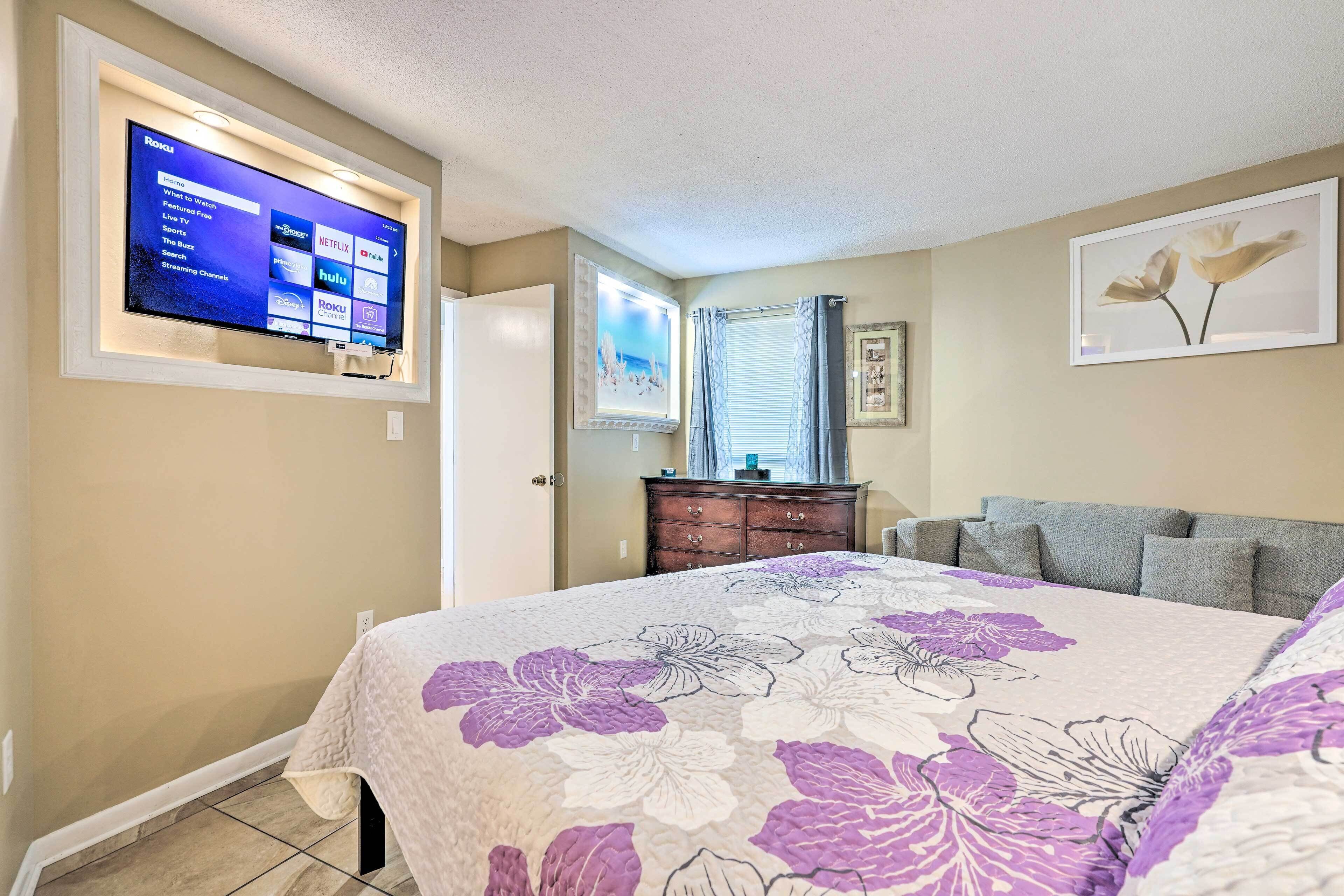 A bedroom with a bed, a TV mounted on the wall, a dresser, and a window with curtains.
