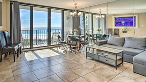 A spacious living area with a balcony, large windows, a sofa, a coffee table, and a dining table with chairs. - Chic PCB Condo w/ Pool Access + Beachfront Balcony (Panama City Beach)
