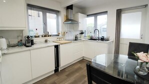 Una cocina moderna con armarios blancos, encimera negra, mesa de comedor de vidrio y una silla negra.