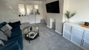 Una sala de estar moderna con un sofá, una mesa de centro de vidrio, un televisor de pantalla plana y un mueble blanco.