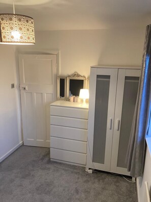 Een slaapkamer met een witte linnenkast, een spiegel, een lamp en een garderobe.