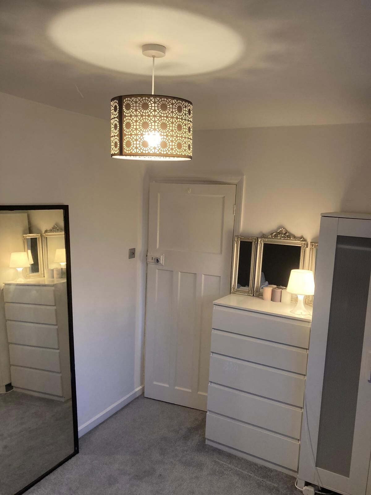 A bedroom with a white dresser, a mirror, a door, and a hanging light fixture.