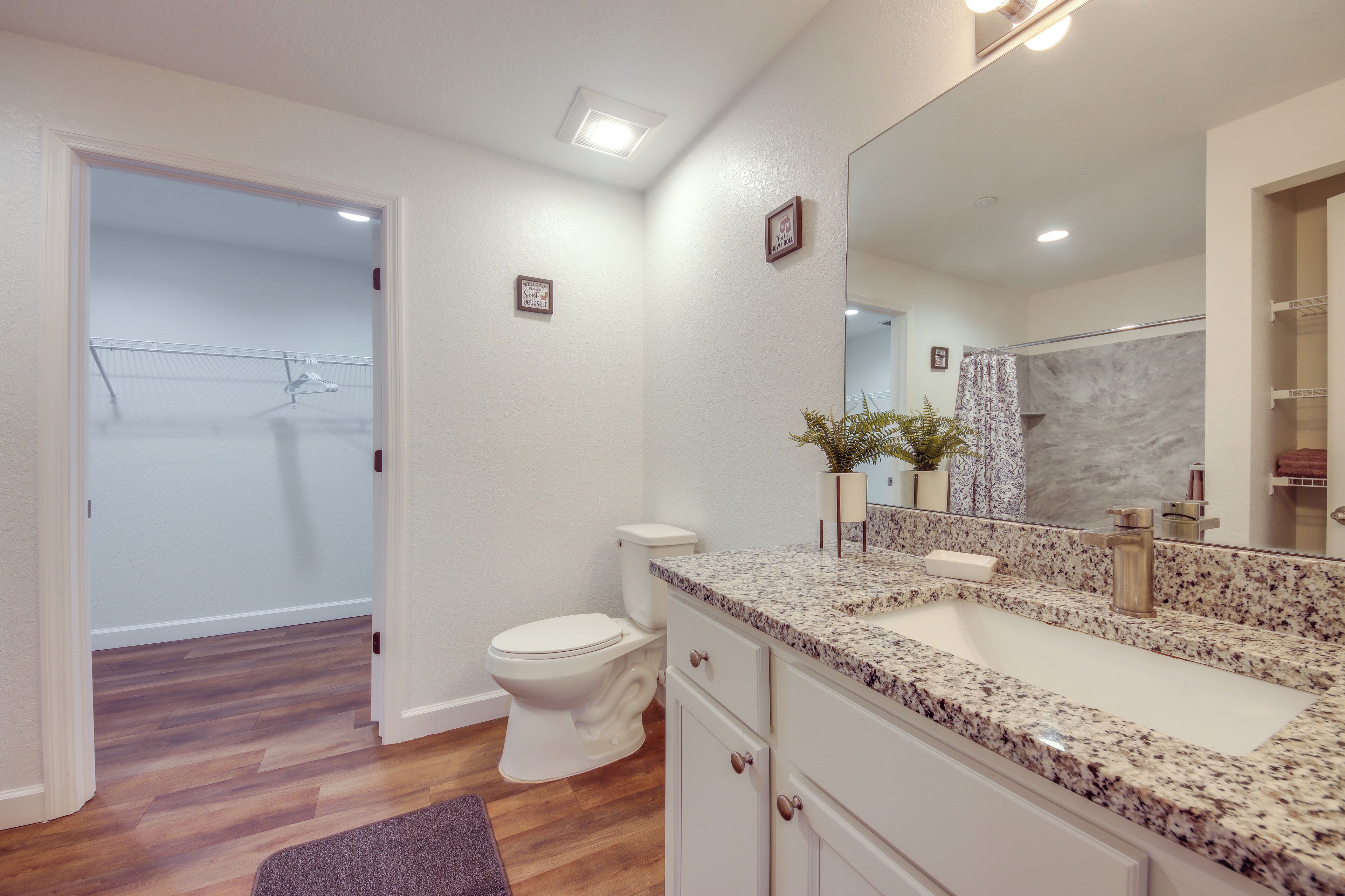 A bathroom with a white toilet, a granite countertop sink, and a large mirror.
