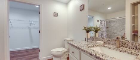 A bathroom with a white toilet, a granite countertop sink, and a large mirror.