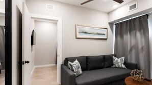 Un salon moderne avec un canapé gris foncé, deux coussins décoratifs à motifs, une table basse en bois et un tableau représentant un paysage, encadré et accroché au mur.