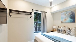 Une chambre à coucher avec un lit, une fenêtre avec des rideaux, une table de chevet avec une lampe et un tableau accroché au mur.