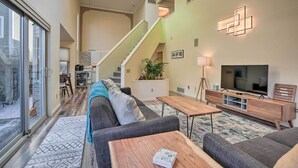 A spacious living area with a large sofa, a coffee table, and a TV stand. A staircase leads to an upper level. - Cozy Anchorage Retreat - Near Hiking & Dtwn! (Anchorage)
