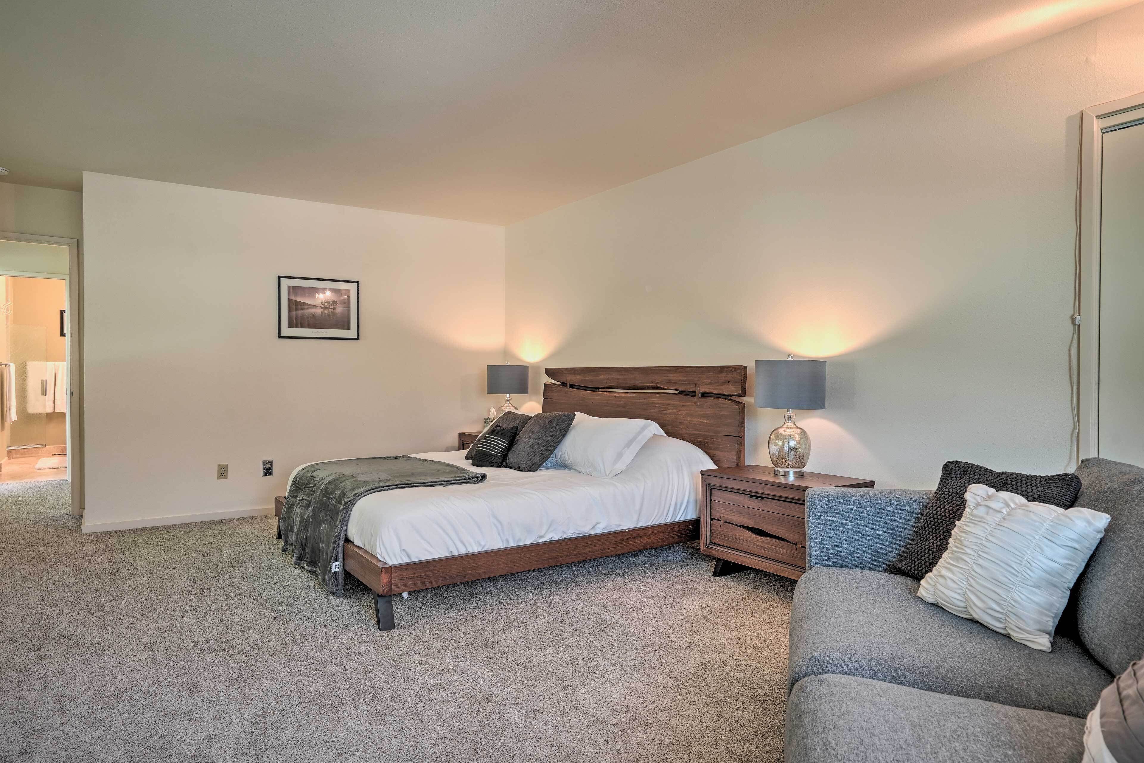 A bedroom with a bed, bedside tables, a nightstand, a couch, and a framed picture on the wall.