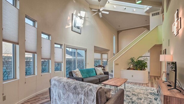 A spacious living room with a gray sofa, a coffee table, and a patterned rug. There is a staircase leading to an upper level, and a ceiling fan is visible. - Cozy Anchorage Retreat - Near Hiking & Dtwn! (Anchorage)