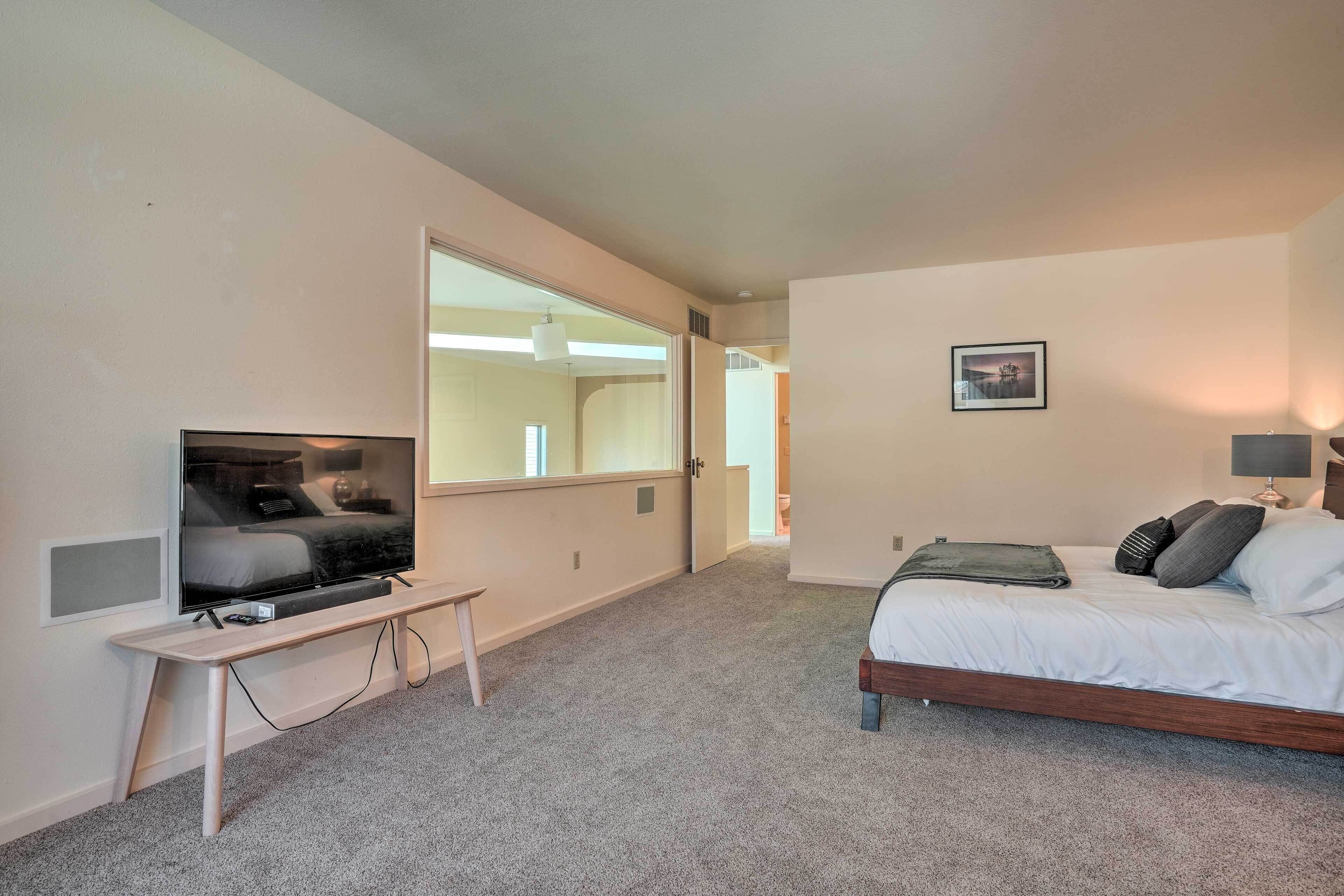 Une chambre d’hôtel moderne avec un grand lit, un téléviseur posé sur un meuble, un bureau et un grand miroir.