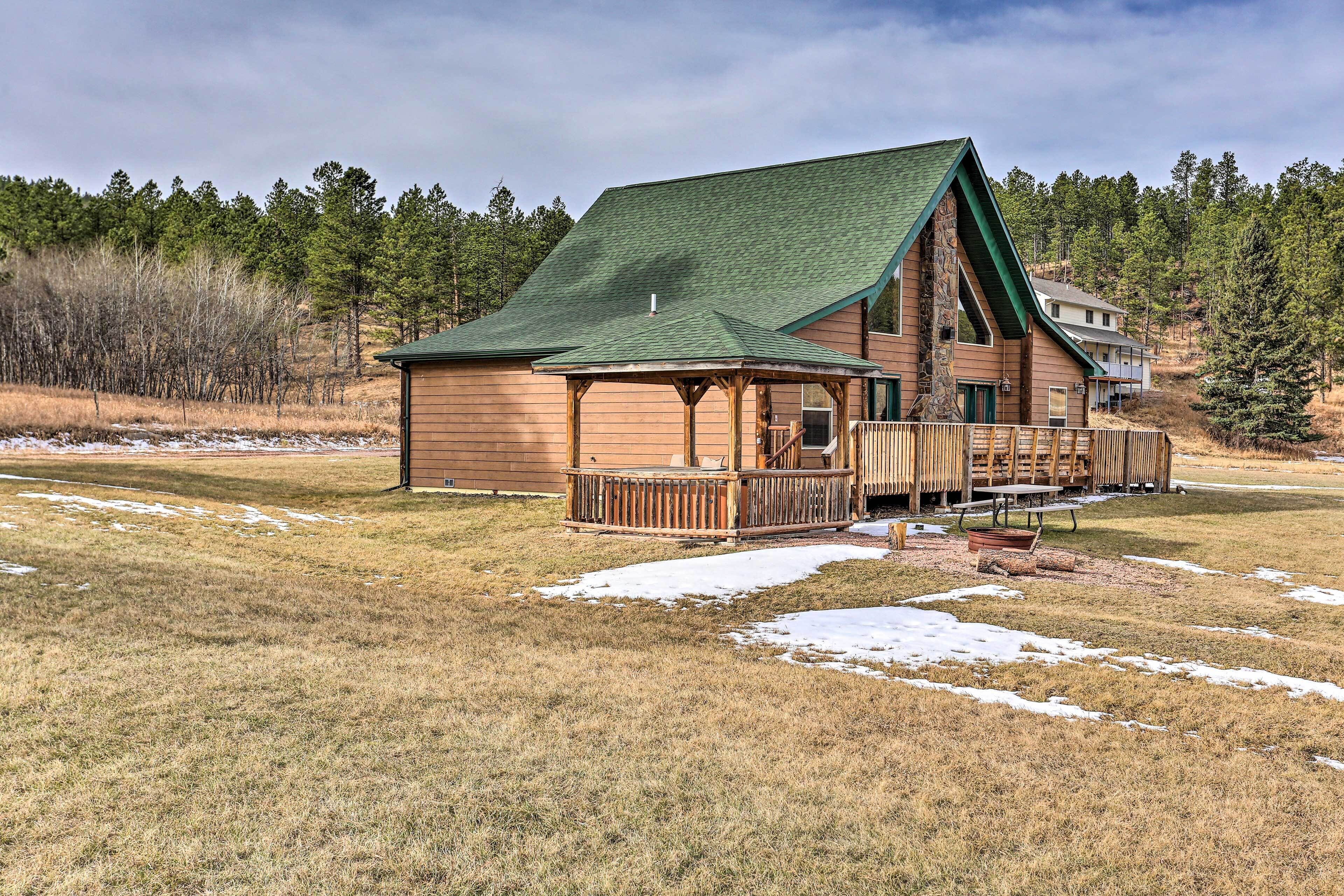 A log cabin with a green roof, a porch, and a picnic table.
