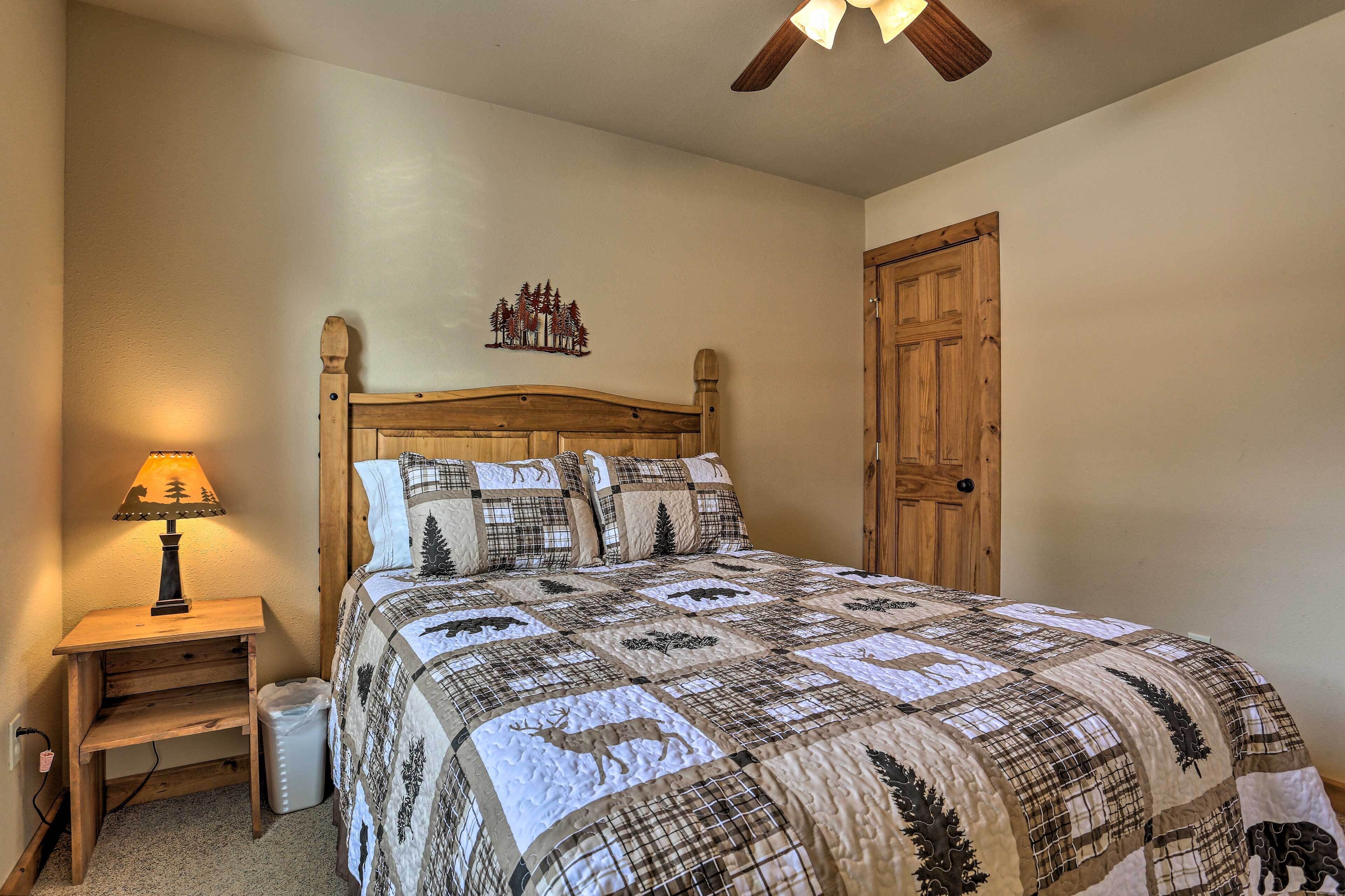 Un dormitorio con una cama de madera, una mesita de noche con lámpara, una puerta de madera y una decoración de árboles en la pared.