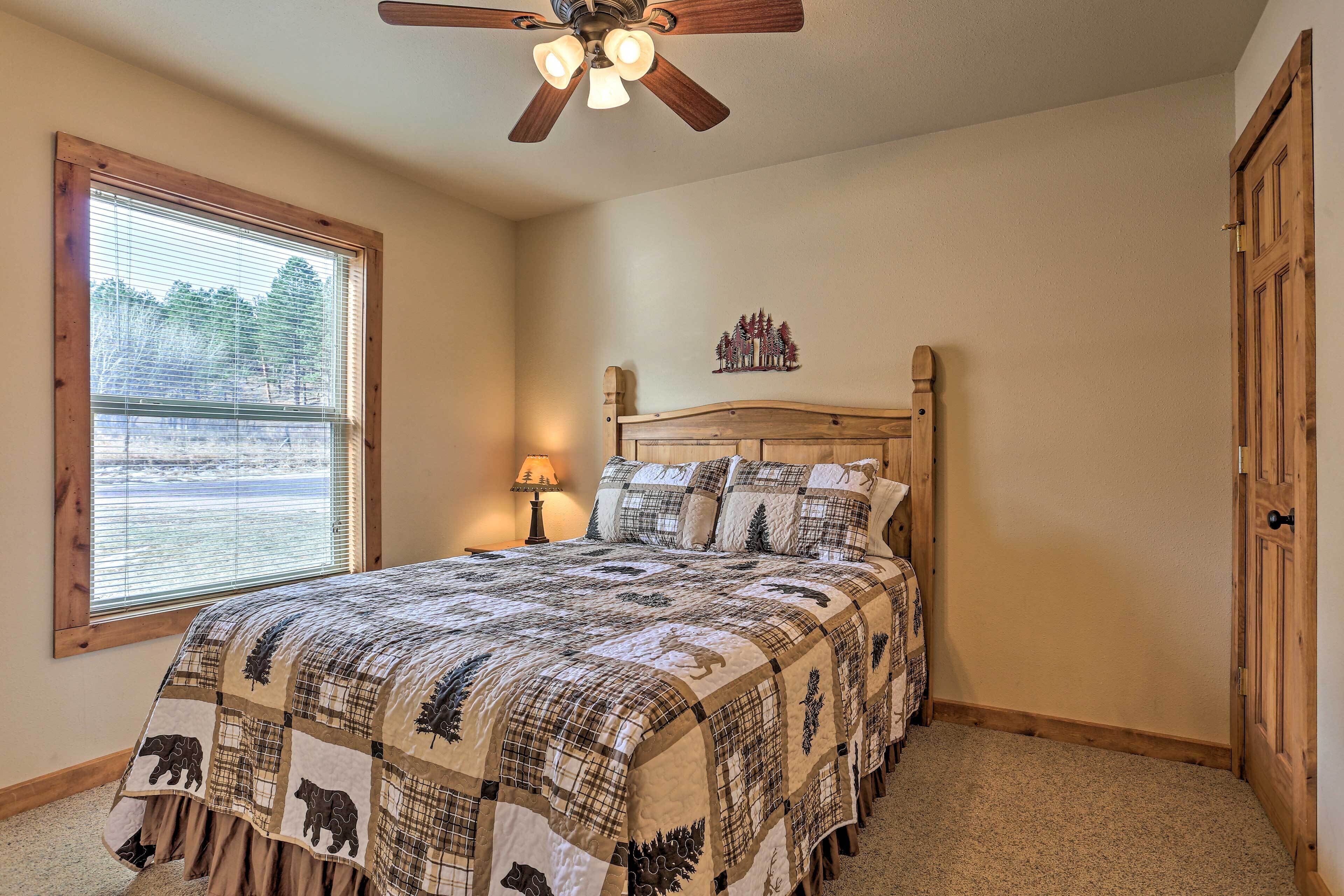 A bedroom with a wooden bed, a ceiling fan, a window with blinds, and a small nightstand with a lamp.