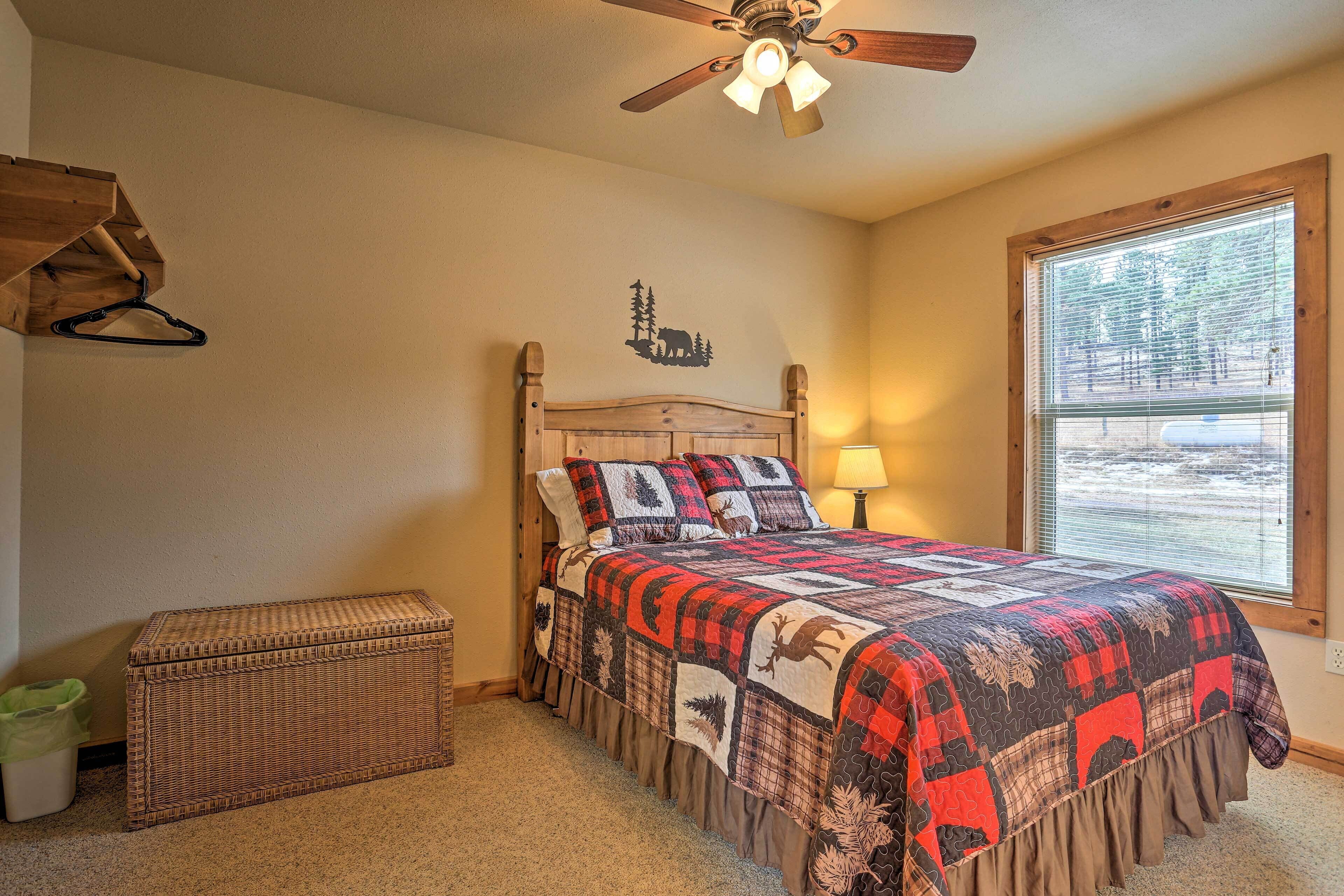 A bedroom with a wooden headboard, a quilted bedspread with animal prints, a wicker chest, and a window with blinds.
