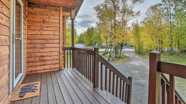 En stuga byggd av trä med en veranda, en dörrmatta och utsikt över en skog med träd i höstfärger.