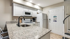 Cocina con armarios blancos, encimera de granito, pileta de acero inoxidable, microondas, estufa y refrigerador.