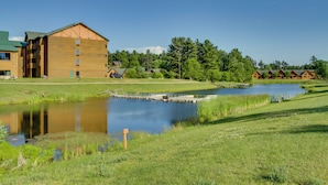 A building with a large wooden facade, a small pond, and a grassy area with trees in the background. - Three Bears Resort Adventure Base w/ Lake Access (Warrens)