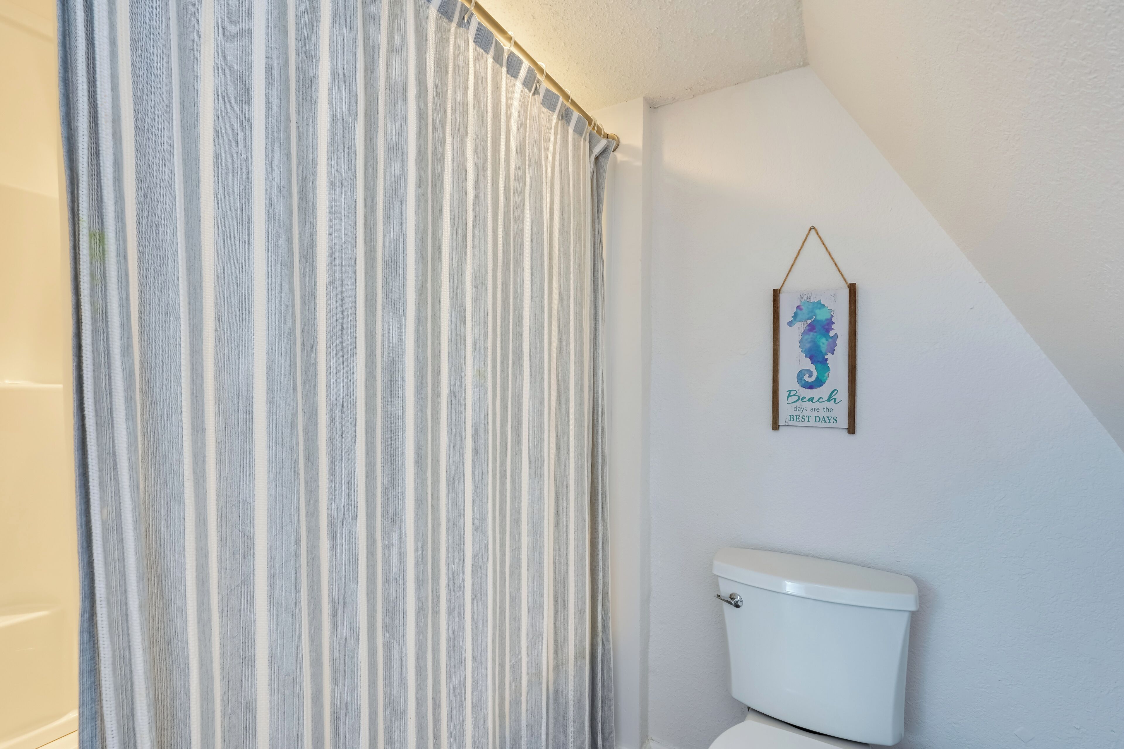 Ein Badezimmer mit gestreiftem Duschvorhang, einer weißen Toilette und einem gerahmten Kunstwerk an der Wand.