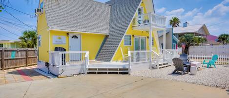A yellow building with a white balcony, a small porch, and outdoor seating.