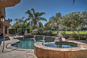Une piscine bordée de pierres, agrémentée d’une petite cascade, et entourée de palmiers et d’un jardin bien entretenu.
