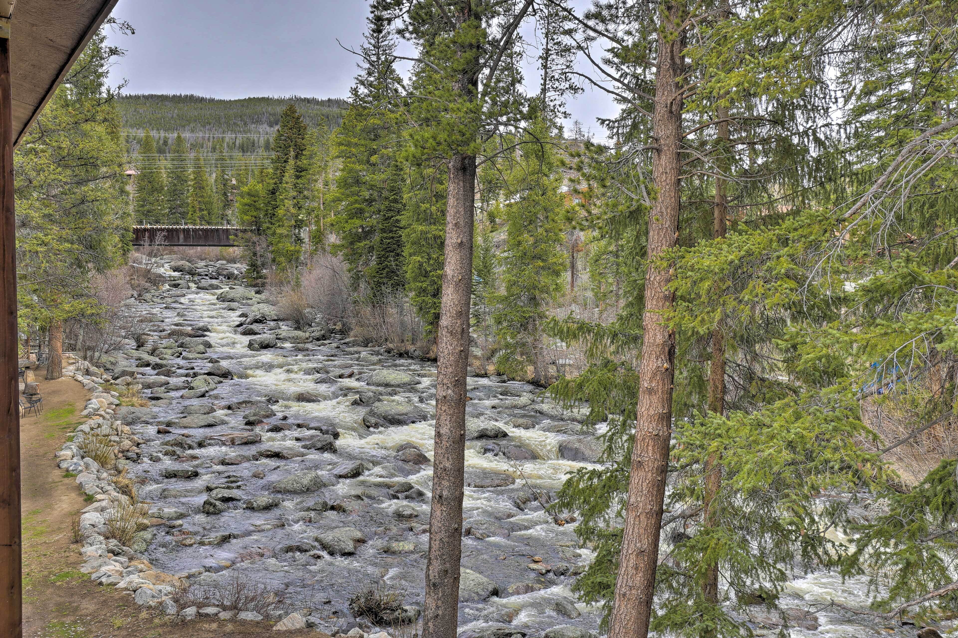A river flowing through a forested area with a wooden structure on the left.