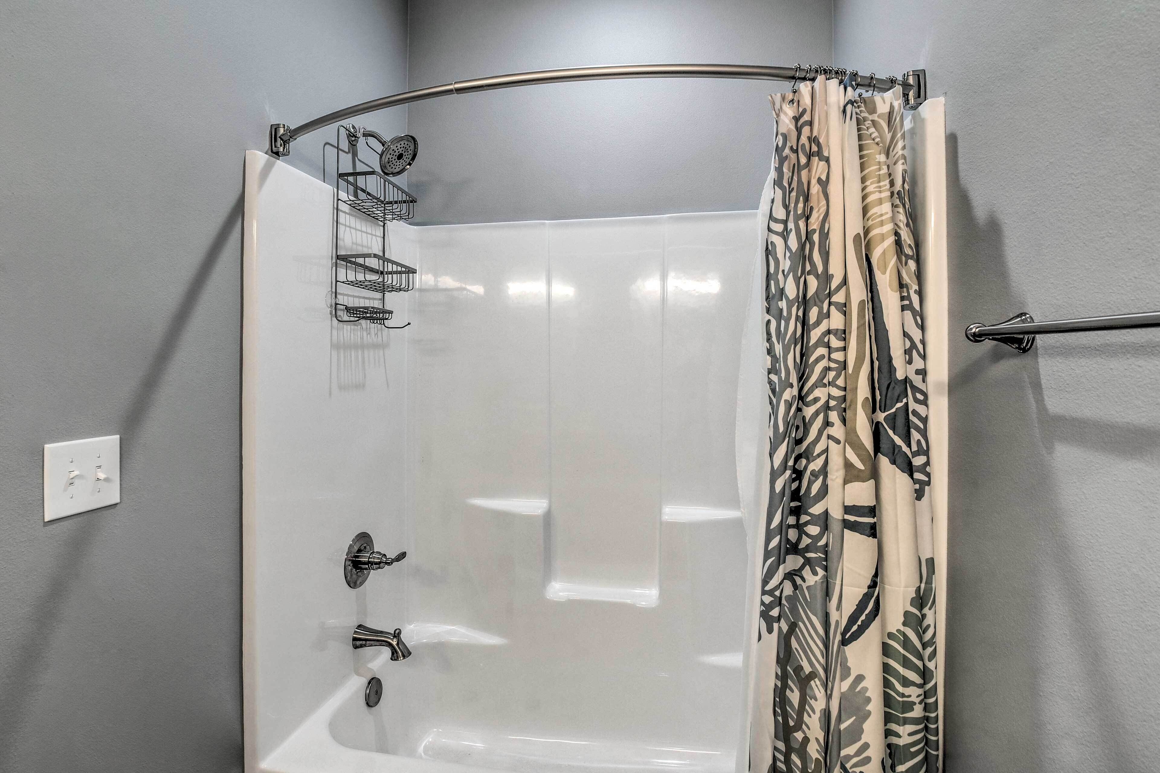 A shower with a curved glass door, a towel rack, and a shower curtain with a leaf pattern.