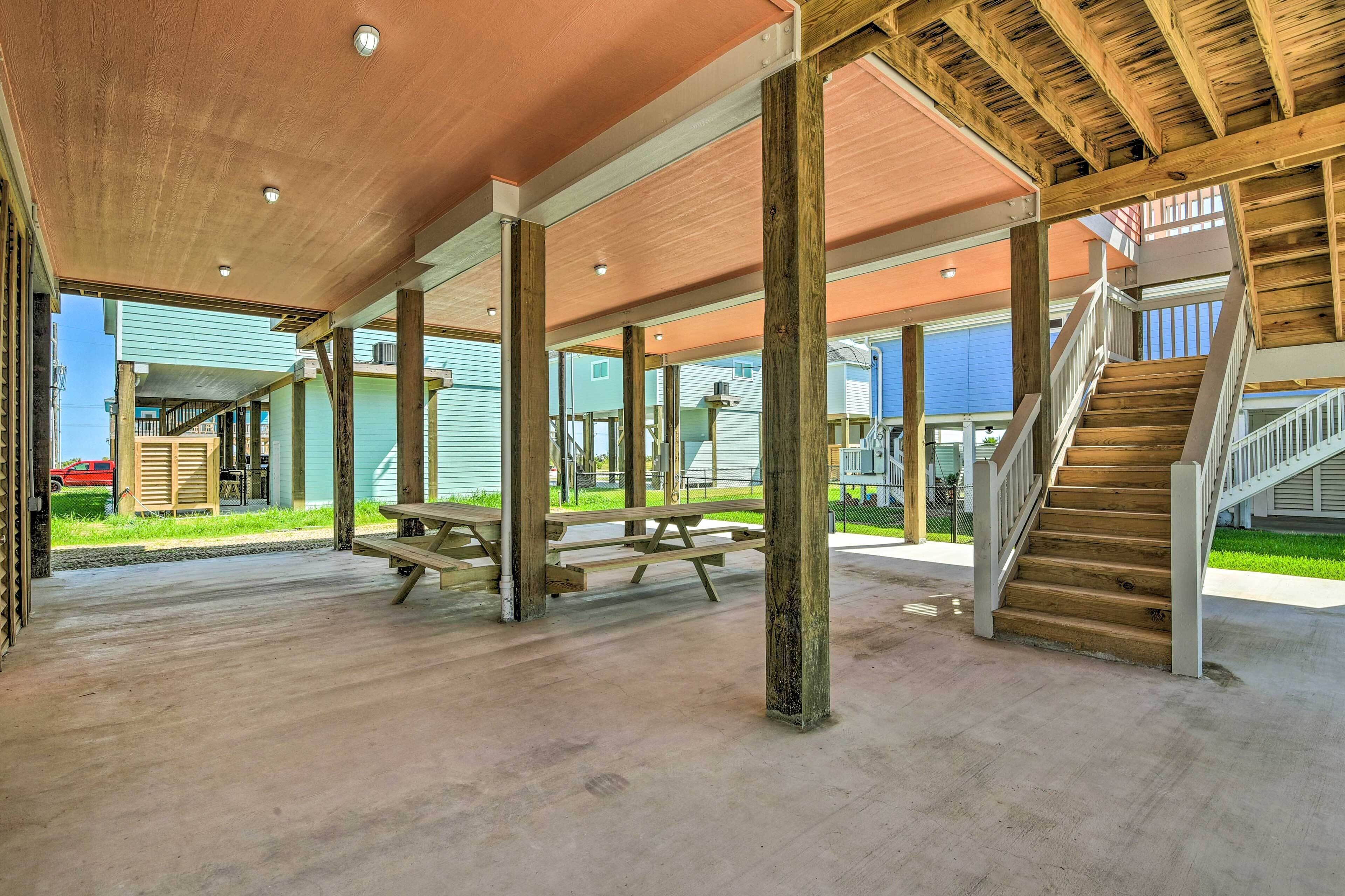 A covered outdoor area with picnic tables, wooden beams, and a staircase leading to an upper level.