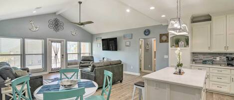 A spacious living area with a dining table, chairs, and a sofa. There is a kitchen with white cabinets and a bar area.