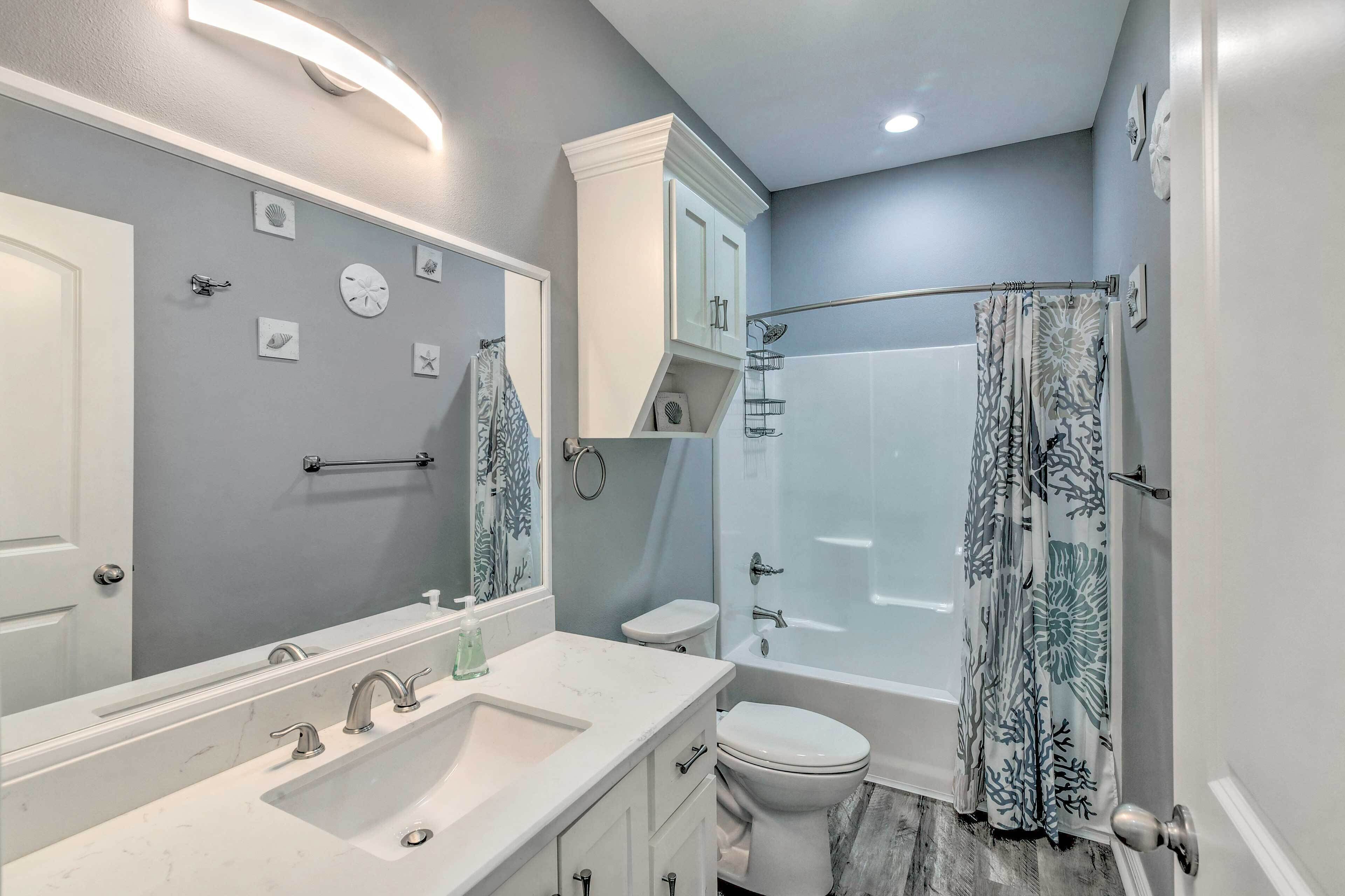 A bathroom with a white vanity, a large mirror, a bathtub, and a shower curtain.