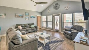 A spacious living room with a grey sofa, a recliner, and a coffee table. There are decorative wall art pieces and a ceiling fan. - Ocean-view Deck, Walk to Shore: Crystal Beach Gem! (Port Bolivar)