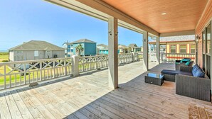 A covered outdoor deck with a wooden floor, a white railing, and a seating area with a sofa and coffee table. - Ocean-view Deck, Walk to Shore: Crystal Beach Gem! (Port Bolivar)