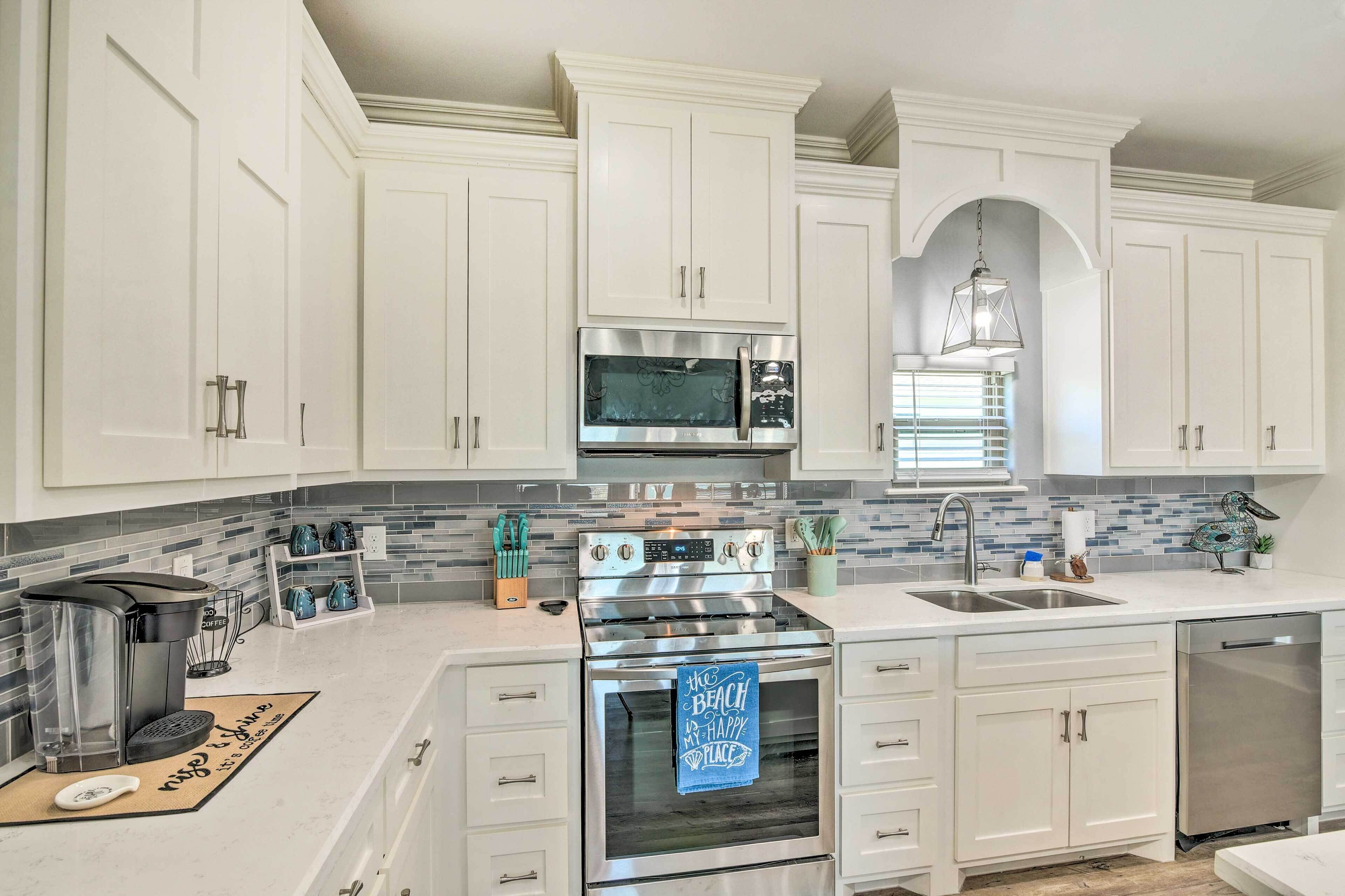 A kitchen with white cabinets, stainless steel appliances, a coffee maker, and a blue towel with a beach message.
