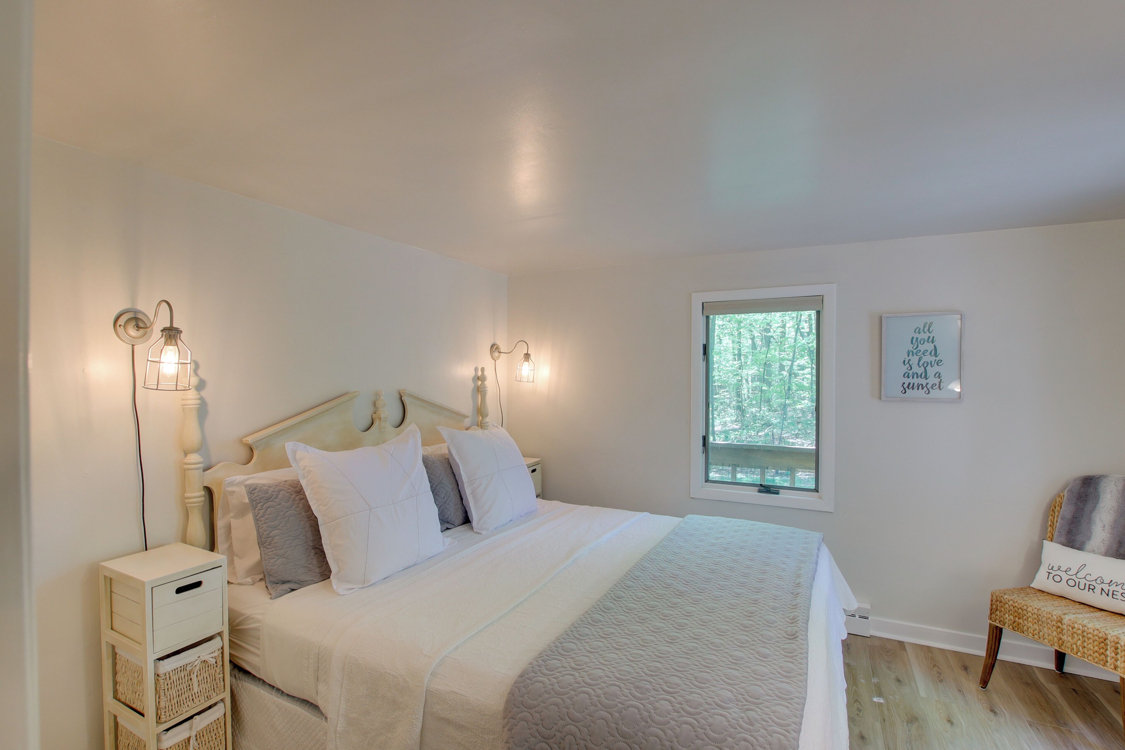 A neatly arranged bedroom with a bed, bedside lamps, a nightstand, a chair, and a window with a view of trees.