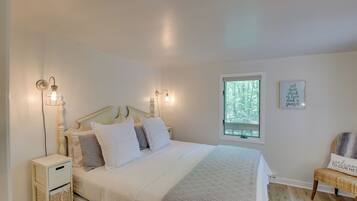 A neatly arranged bedroom with a bed, bedside lamps, a nightstand, a chair, and a window with a view of trees.