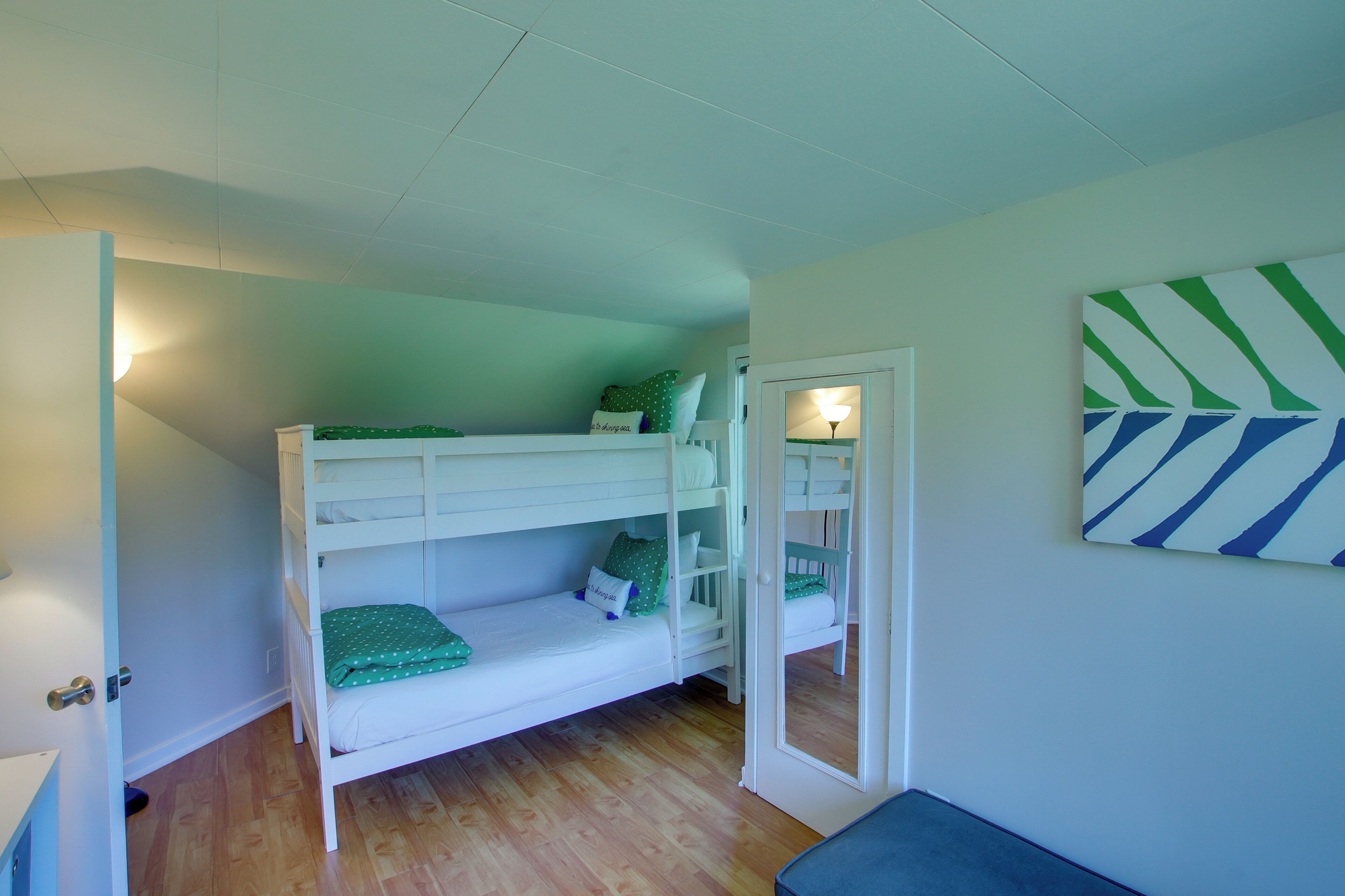 A bunk bed room with a door leading to another room, a wall-mounted light, and a geometric wall decoration.