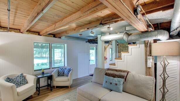 A cozy living room with a wooden ceiling, a beige sofa, a white armchair, and a small table.