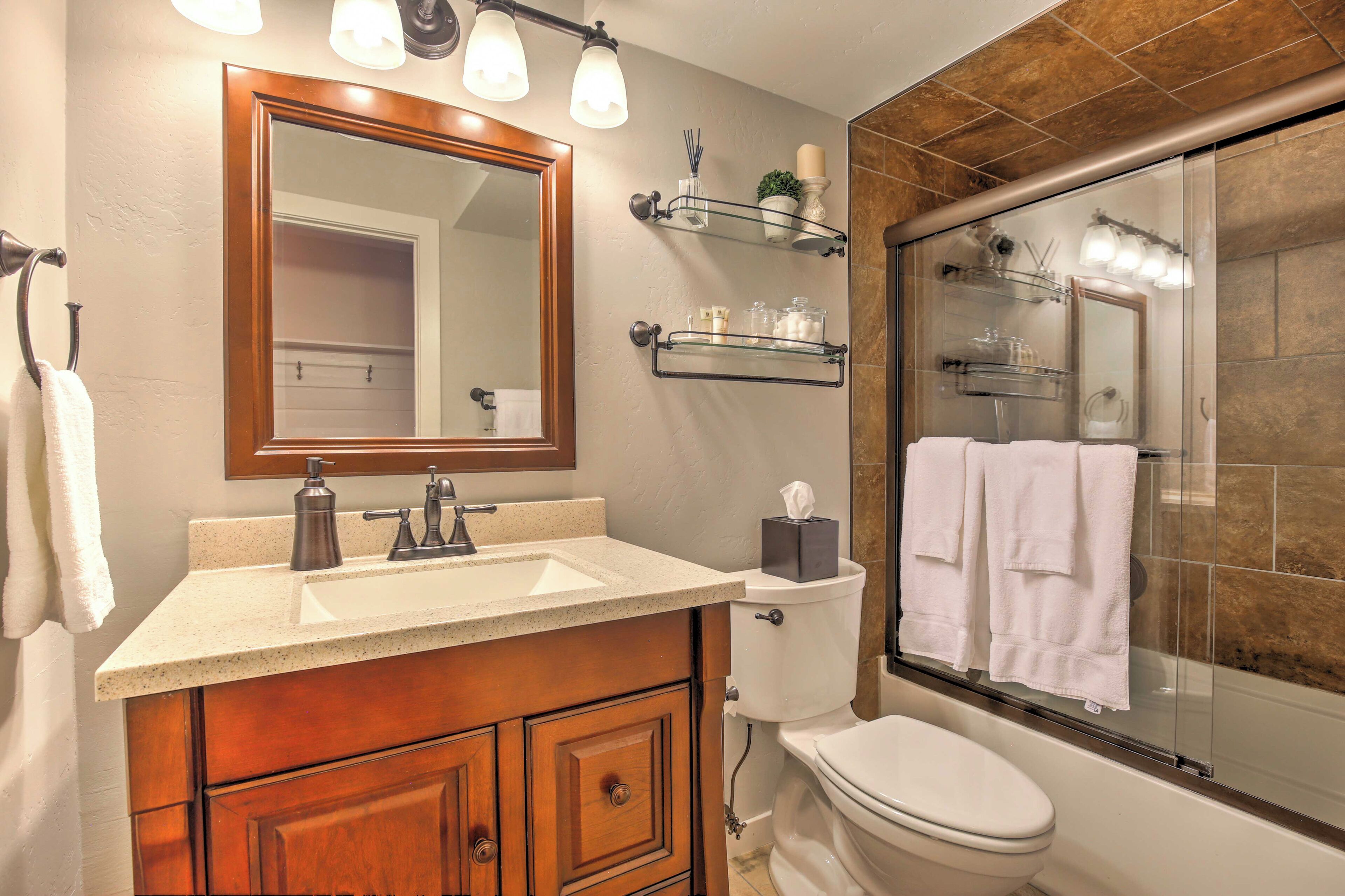 A bathroom with a wooden vanity, a large mirror, a toilet, and a glass-enclosed shower area.