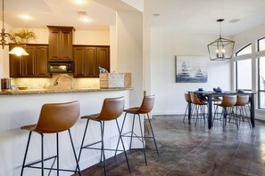 A modern kitchen with dark wooden cabinets, a stainless steel sink, and a built-in microwave. There are bar stools and a dining table with chairs. - Stylish Home w/ Hot Tub ~ 4 Mi to Canyon Lake (Canyon Lake)