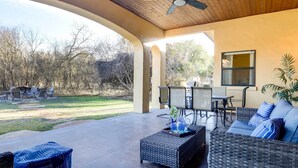 A covered patio area with outdoor furniture, including a sofa and chairs, a dining table, and a ceiling fan.