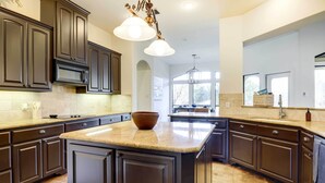 A modern kitchen with dark cabinetry, a central island, and a large window providing natural light.