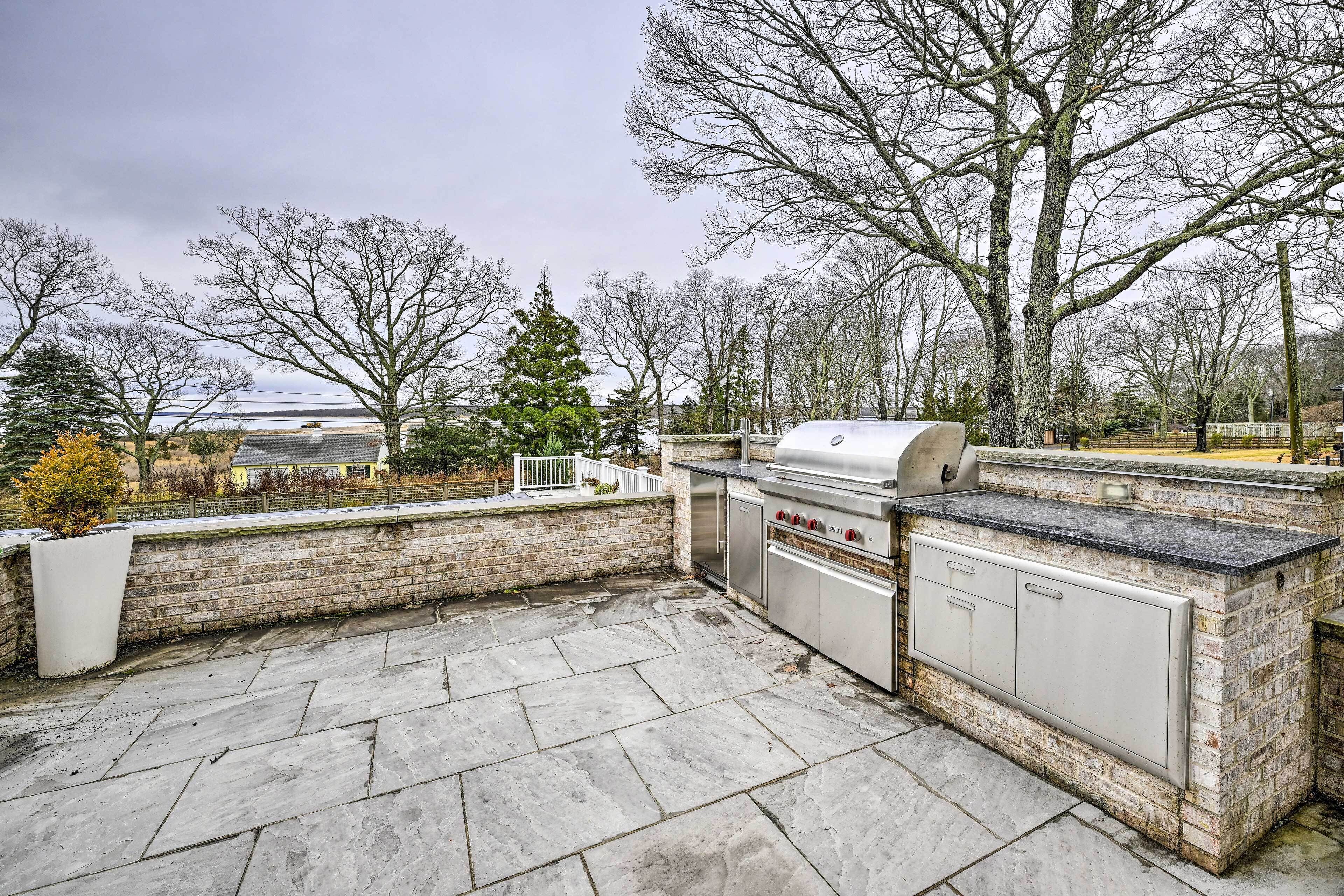 An outdoor patio with a stone floor, a grill, and a brick wall.