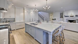 Una cocina moderna con armarios blancos, una isla grande con taburetes y una escalera que lleva al piso superior.