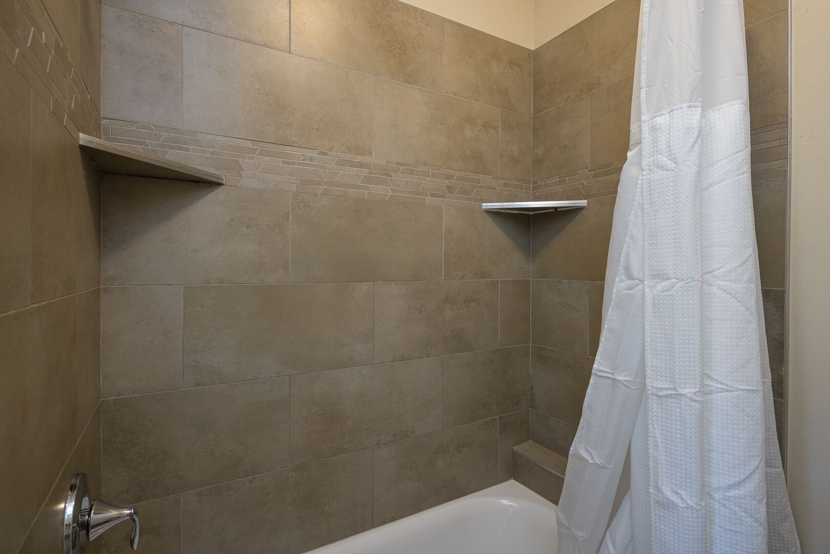 A bathroom with beige tiles, a white bathtub, and a shower curtain.