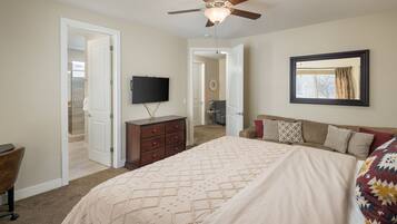 A bedroom with a bed, dresser, TV, and a ceiling fan.