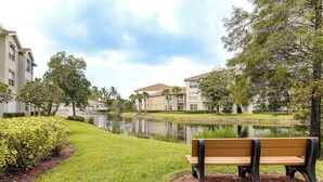 A bench in a park with a pond and buildings in the background. - Work, Swim + Play in Ft Myers: Resort Condo Stay! (Fort Myers)