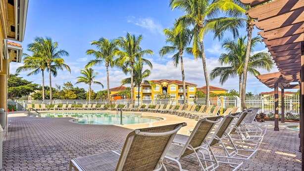 A poolside area with lounge chairs, palm trees, and a building in the background. - Work, Swim + Play in Ft Myers: Resort Condo Stay! (Fort Myers)