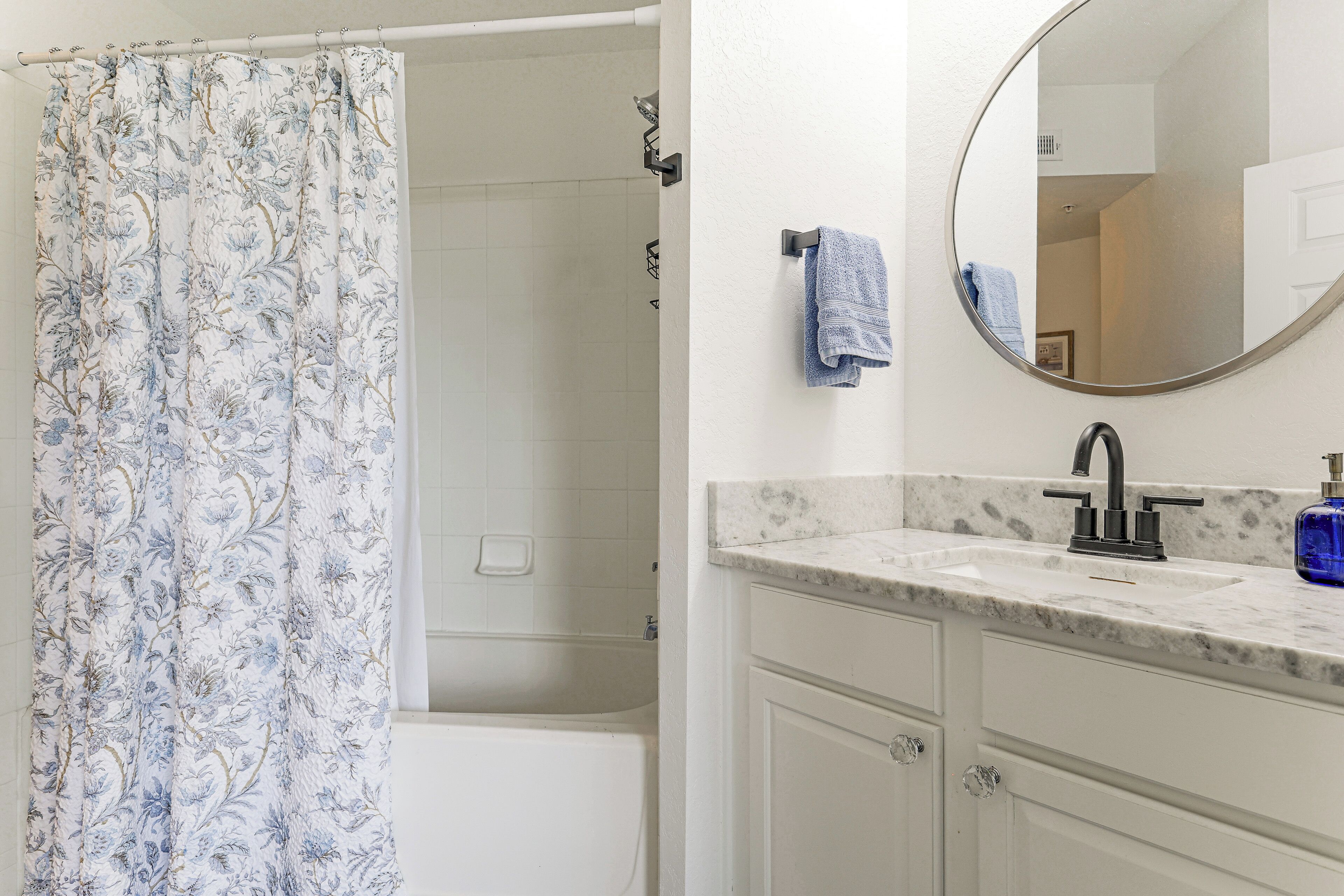 A bathroom with a shower curtain, a sink with a mirror, and a towel hanging on the wall.