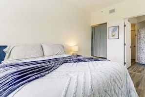 Un lit recouvert d’une couverture à rayures blanches et bleues, une lampe de chevet et une porte donnant sur une autre pièce.